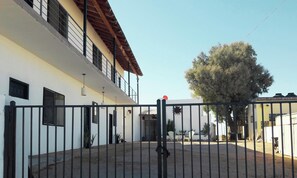 A gated courtyard with a building featuring multiple windows and a large tree.