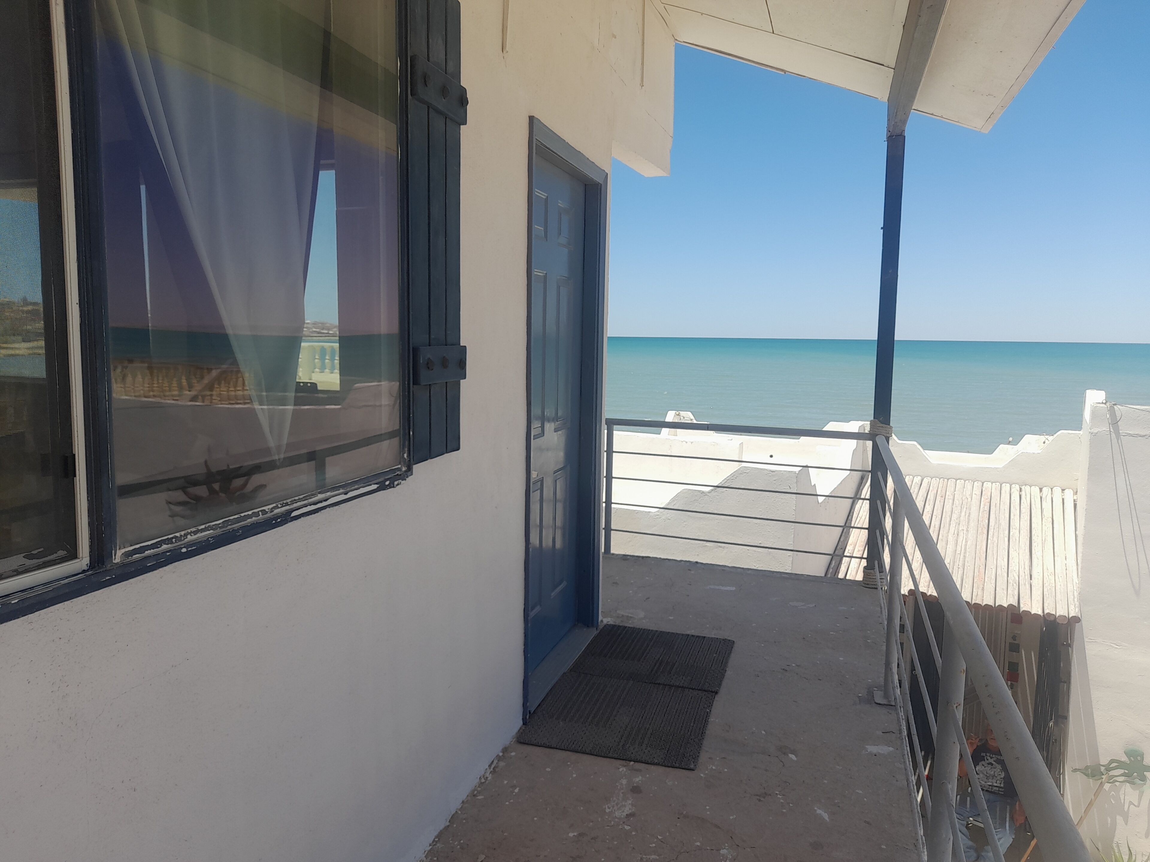 Een balkon met uitzicht op zee, een deur en een raam met gordijnen.