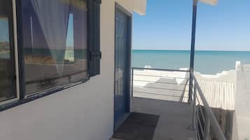 Een balkon met uitzicht op zee, een deur en een raam met gordijnen.