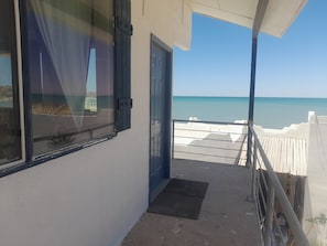 A balcony with a view of the sea, a door, and a window with curtains.