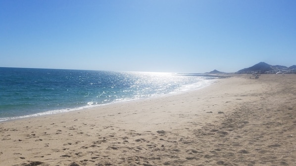 Una playa con huellas, cielo despejado y montañas a lo lejos.