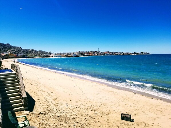 A beach with a clear view of the sea, a sandy shore, and a row of buildings in the background.