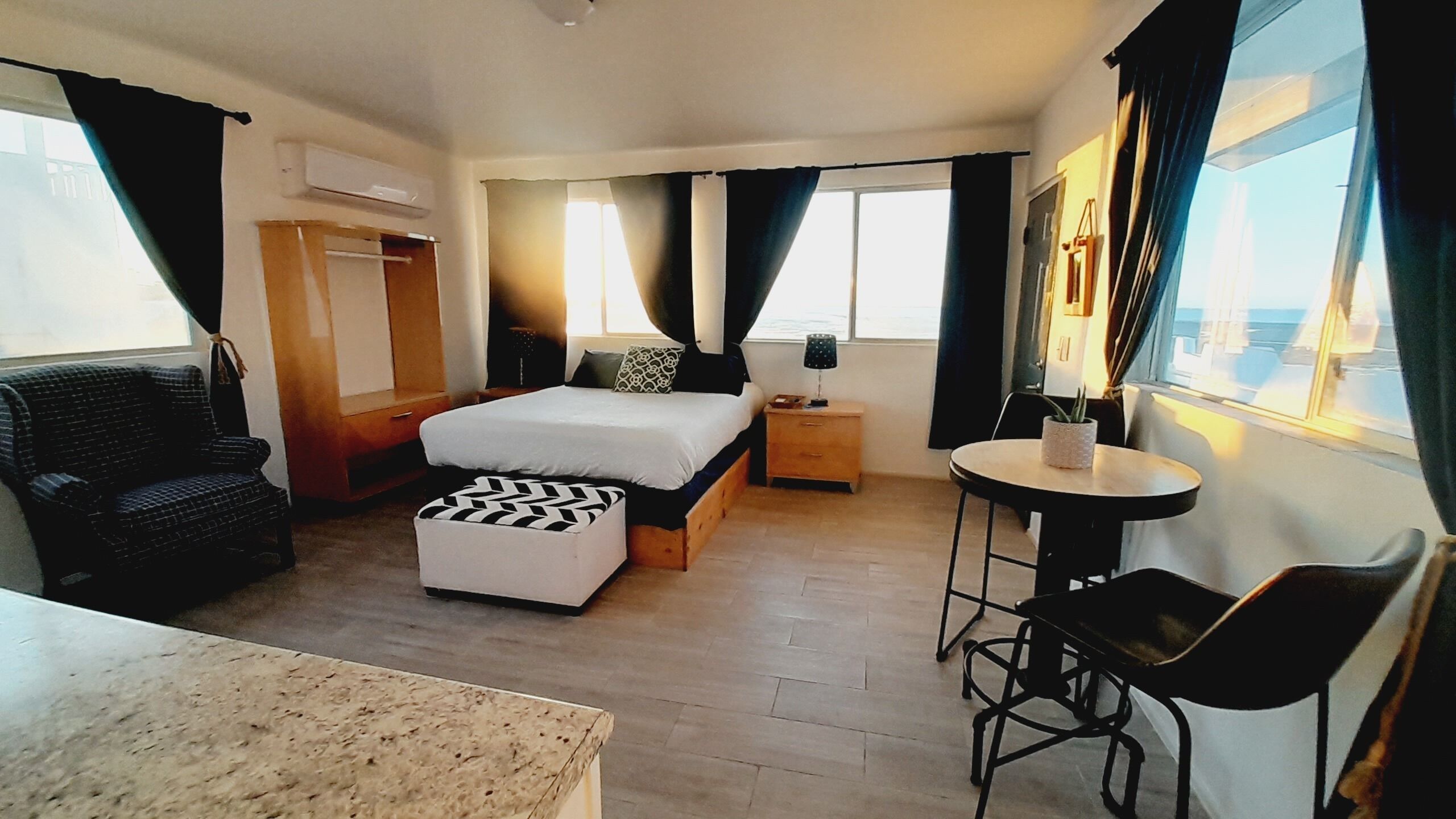 A hotel room with a bed, a desk, a chair, a small table, and a window with curtains.