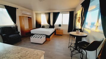 A hotel room with a bed, a desk, a chair, a small table, and a window with curtains.