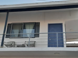 Un edificio con balcón, una puerta azul y dos bancos.