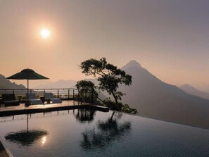 A serene infinity pool with a mountain backdrop, lounge chairs, and a shaded area. - Green Acres Leisure Resort (Kadigamuwa)
