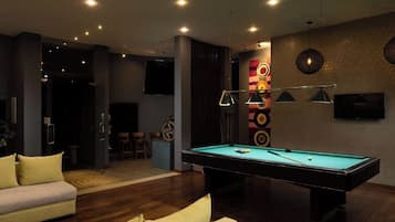 Una sala de estar moderna con mesa de billar, sofás y televisor montado en la pared.