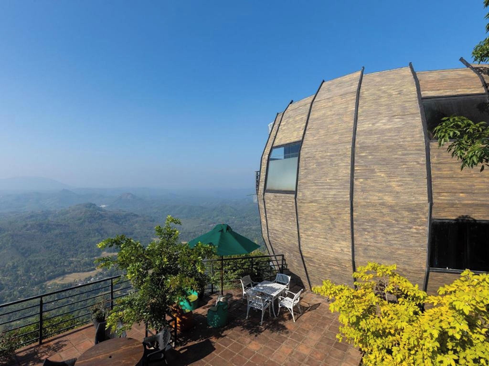 Un edificio moderno con fachada de madera curva, asientos al aire libre y vistas a un paisaje montañoso.