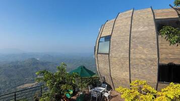Un edificio moderno con fachada de madera curva, asientos al aire libre y vistas a un paisaje montañoso.