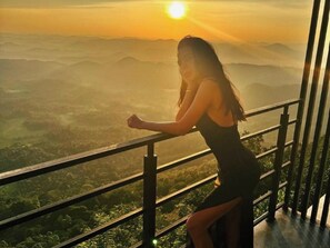 A person leaning on a balcony railing overlooking a mountainous landscape during sunset. - Green Acres Leisure Resort (Kadigamuwa)