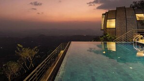Um edifício moderno com piscina ao anoitecer, com vista para uma paisagem montanhosa.