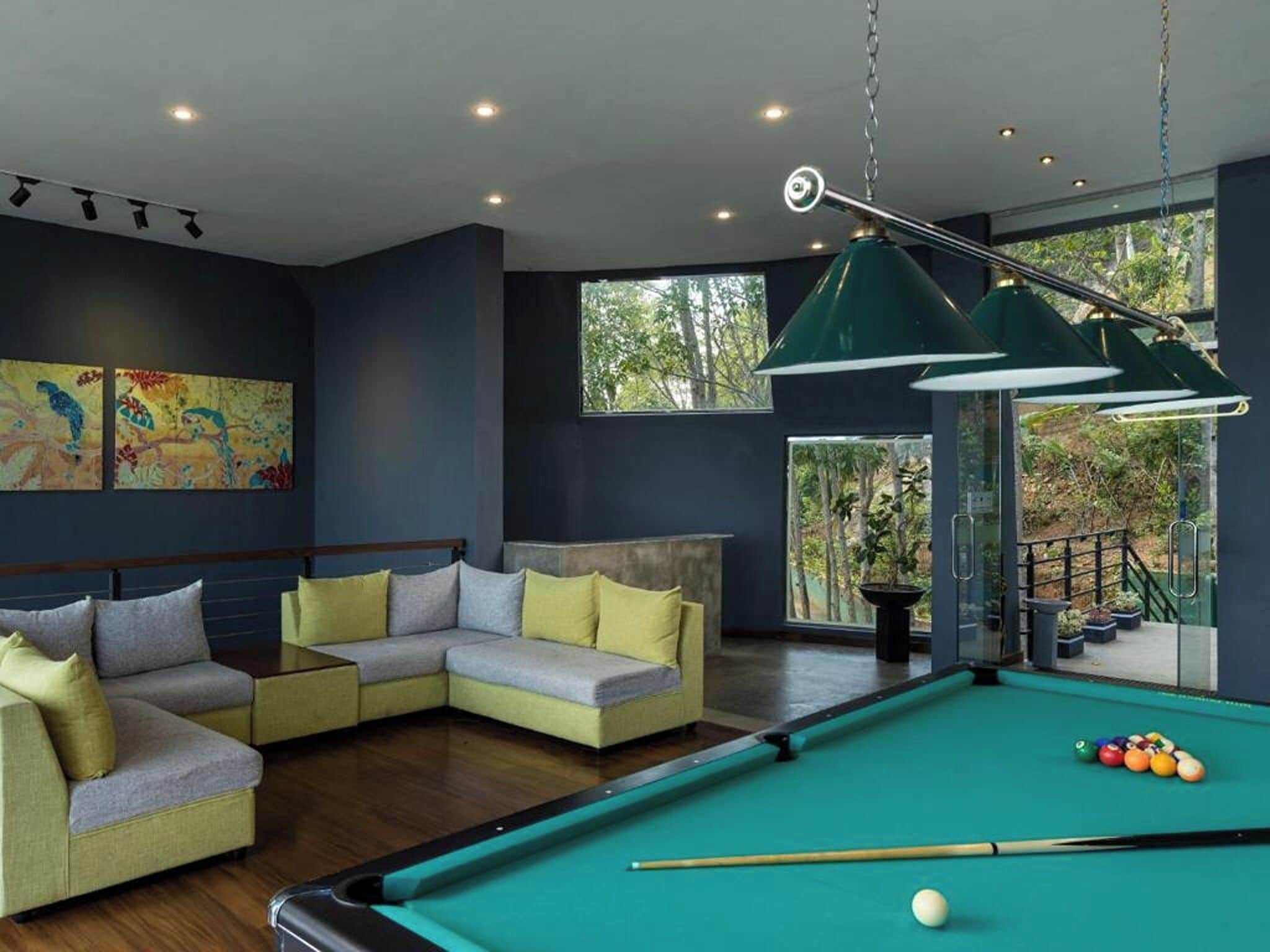 Una sala de estar moderna con mesa de billar, sofá modular y un ventanal con vistas a árboles.