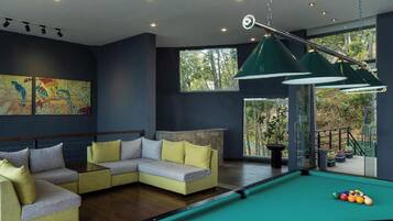 Una sala de estar moderna con mesa de billar, sofá modular y un ventanal con vistas a árboles.