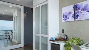 Quarto de hotel moderno com varanda, porta deslizante, pequeno kitchenette e área de refeições.
