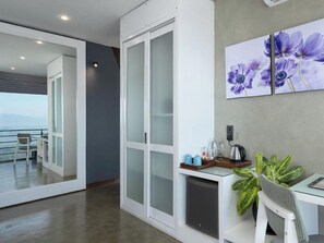 A modern hotel room with a balcony, a sliding door, a small kitchenette, and a dining area.