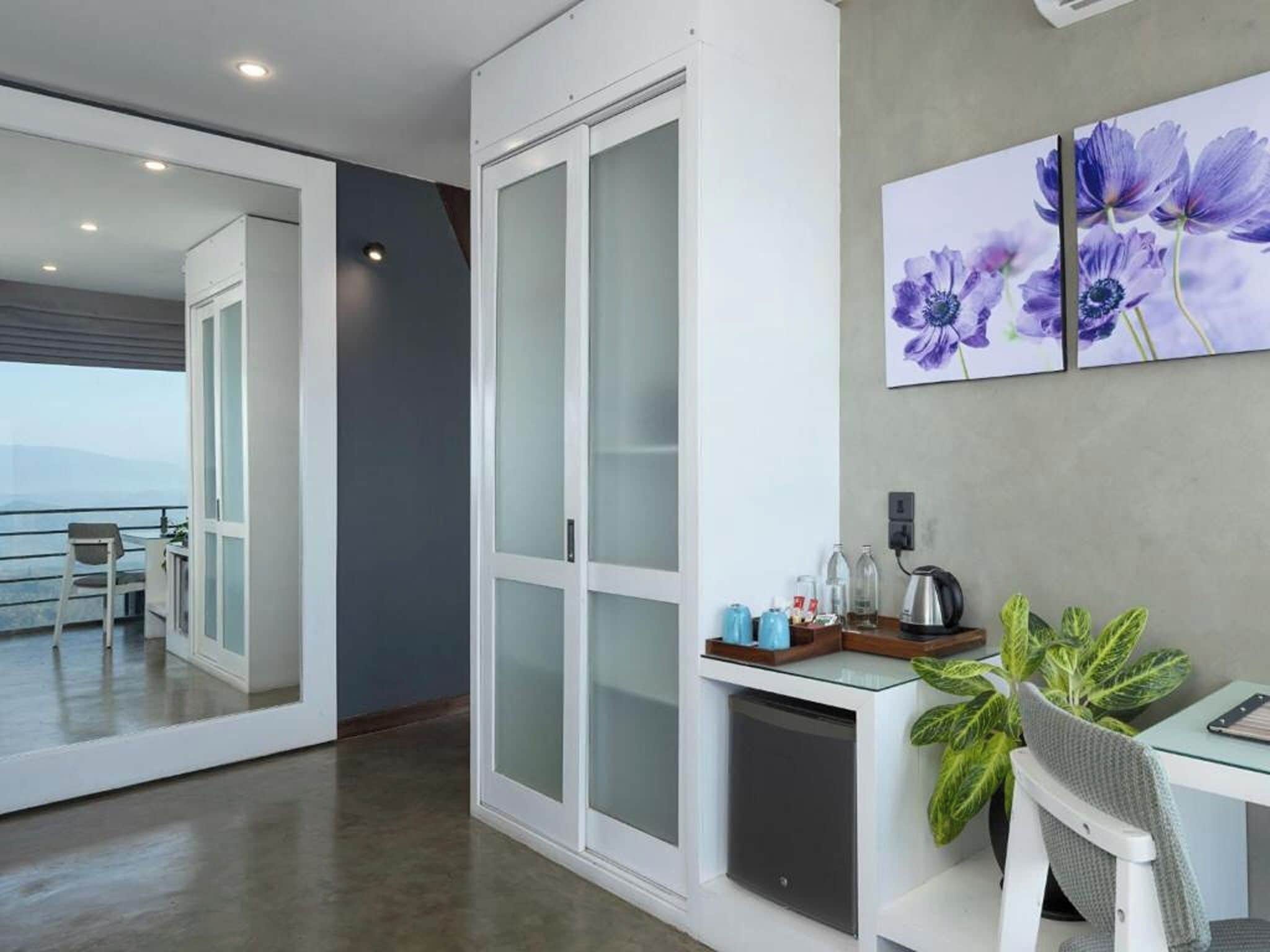 A modern hotel room with a balcony, a dining area with a plant, and a coffee station.