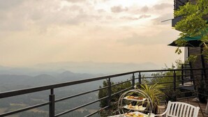 Uma mesa posta com chá e um suporte de sobremesas em um balcão com vista para uma paisagem montanhosa.