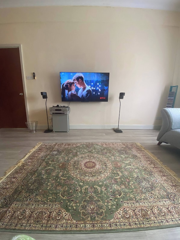 Una sala de estar con un televisor de pantalla plana grande montado en la pared, un tapete estampado en el suelo y un sofá gris.