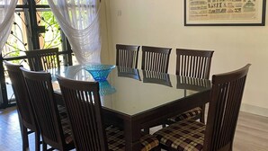 A dining area with a glass-top table, six wooden chairs, a blue glass bowl, and a framed cityscape picture on the wall. - Urban Living in Kampung Setting (Kuching)