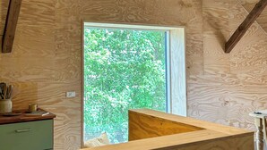 A wooden interior with a sloped ceiling, a hanging light fixture, a window with a view of trees, and a counter with a cup and utensils. - Unplug in rustic barn idyll near Jels (Sommersted)