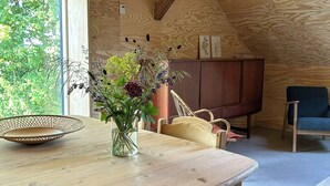 A wooden interior with a dining table, chairs, a vase with flowers, and a television. - Unplug in rustic barn idyll near Jels (Sommersted)