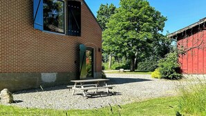 A brick building with a sloped roof, a wooden bench, and a large tree in the background. - Unplug in rustic barn idyll near Jels (Sommersted)