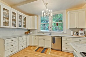 A kitchen with white cabinetry, a chandelier, a window with a view of greenery, and a wooden floor. - Terrific 6-bedroom house with AC in peaceful Historic downtown Palo Alto (Palo Alto)