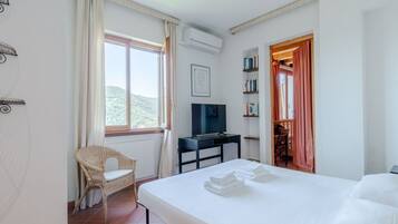 A hotel room with a bed, a television, a chair, a desk, and a bookshelf.