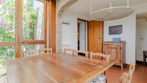 Een eetruimte met een houten tafel en stoelen, een hanglamp en uitzicht op groen.