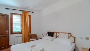 Een slaapkamer met een bed, een stoel, een raam met gordijnen, een radiator en een houten deur.