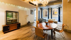 Un coin repas avec une table ronde, des chaises en osier, un buffet en verre contenant des verres à vin et un lustre.