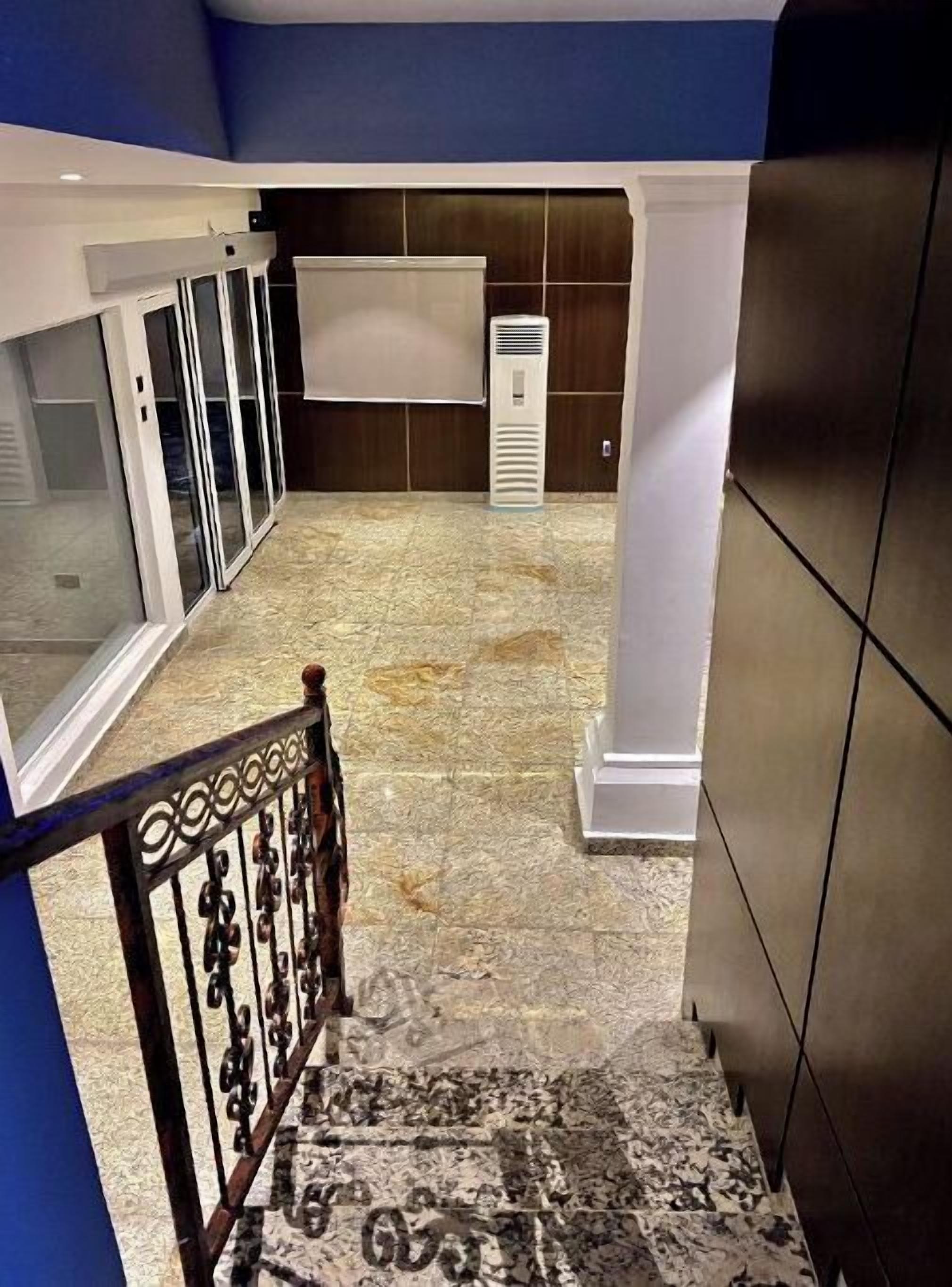 Un pasillo con piso de baldosas, una unidad de aire acondicionado blanca y un objeto blanco montado en la pared.