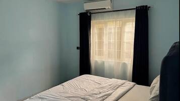 Una habitación con cama, aire acondicionado, ventana con cortinas y una vista parcial de una pared.