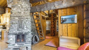 A rustic interior with a stone fireplace, wooden beams, a wooden ladder, a television, and a sofa. - Luostonseita 2 by Interhome (Sodankylä)