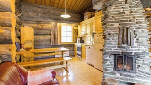 A cozy cabin interior with a stone fireplace, wooden furniture, and a kitchen area. - Luostonseita 2 by Interhome (Sodankylä)