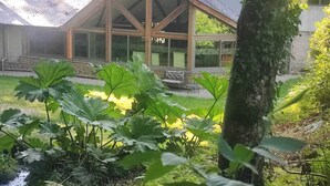 A building with a sloped roof and large windows, surrounded by lush greenery and a small pond. - Large vacation rental for 15 people with a private pond • 45 minutes from Mont Saint-Michel (Landéan)