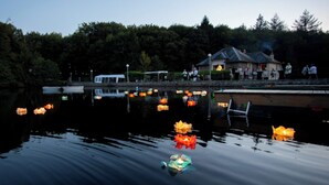 A calm lake with floating lanterns, a dock, and a building with people on the shore. - Large vacation rental for 15 people with a private pond • 45 minutes from Mont Saint-Michel (Landéan)