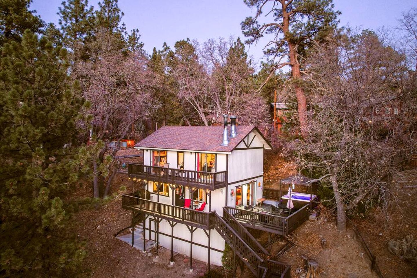 A two-story cabin with a balcony, surrounded by trees.