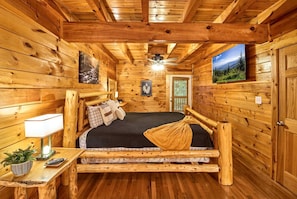 A log cabin bedroom with a bed, a nightstand, a lamp, and a television. - Spacious Cabin Retreat with Hot Tub & Games near Dollywood in Pigeon Forge, TN (Pigeon Forge)