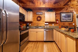 A kitchen with wooden cabinets, a stainless steel refrigerator, a dishwasher, granite countertops, and a wooden floor. - Spacious Cabin Retreat with Hot Tub & Games near Dollywood in Pigeon Forge, TN (Pigeon Forge)