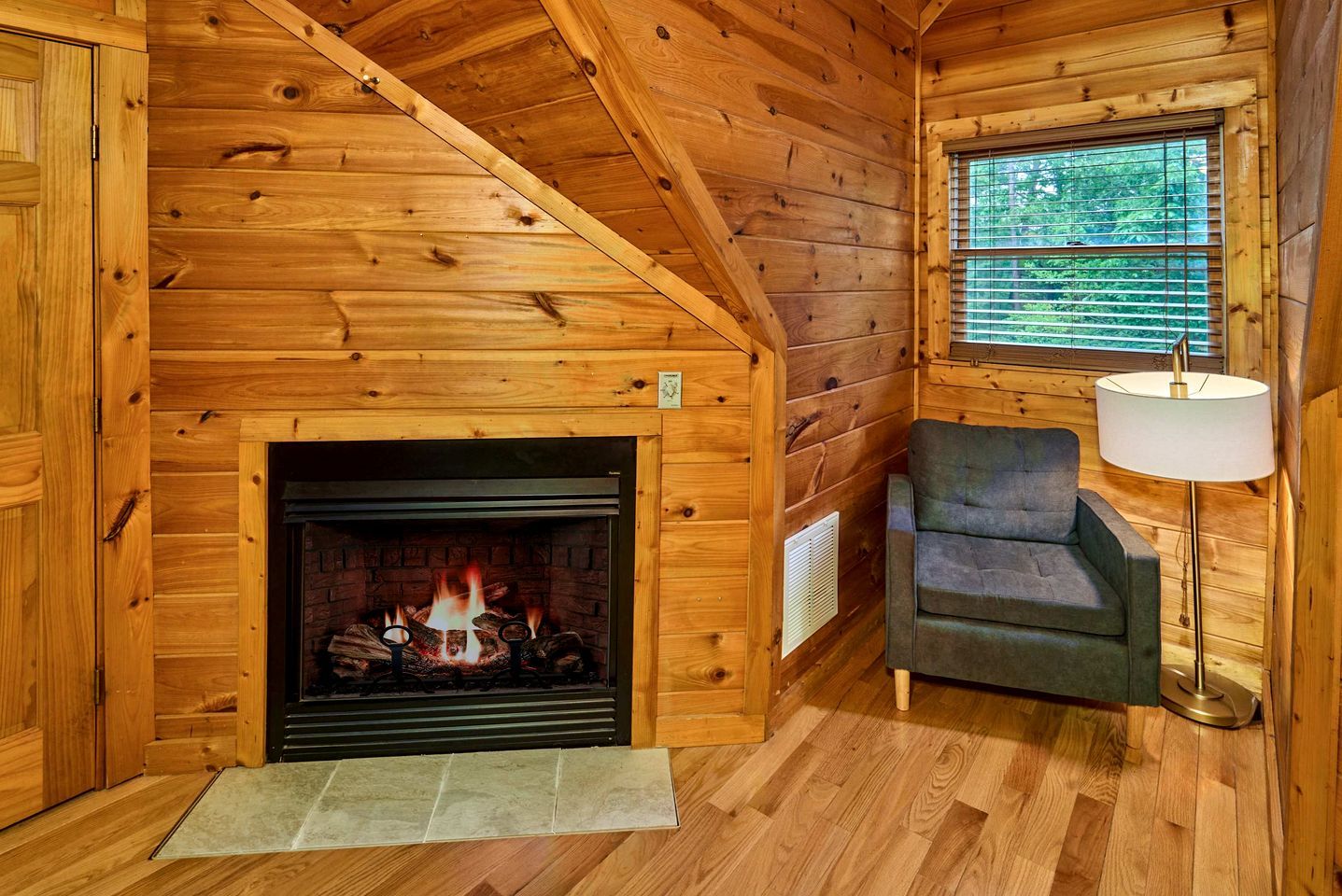 L’intérieur d’une cabane en rondins, avec une cheminée, un canapé et une fenêtre avec des stores.