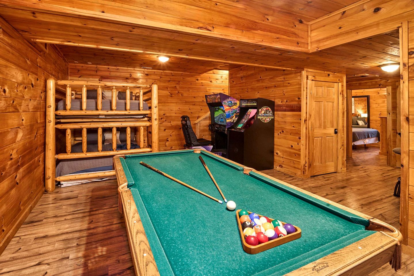 Une table de billard avec un queue, un porte-billes et une borne d’arcade dans une pièce en bois.