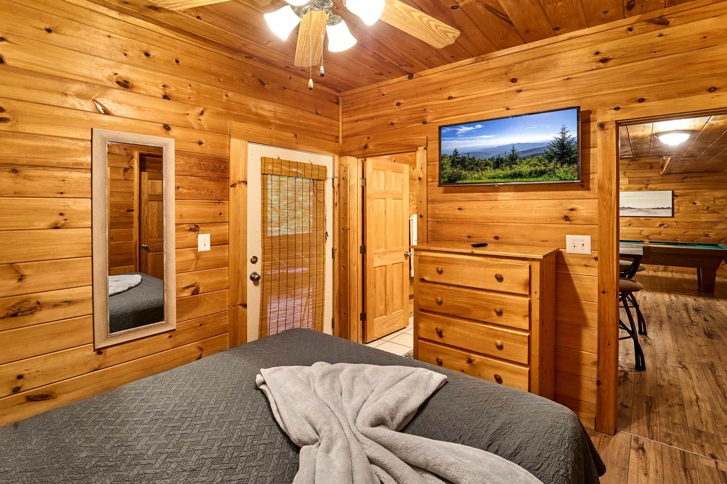 Une chambre rustique en bois, avec un lit, une commode, un miroir et un téléviseur fixé au mur.