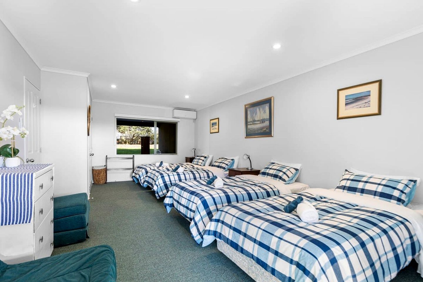 A hotel room with four beds, a desk, a chair, a dresser, and a window with a view of greenery.