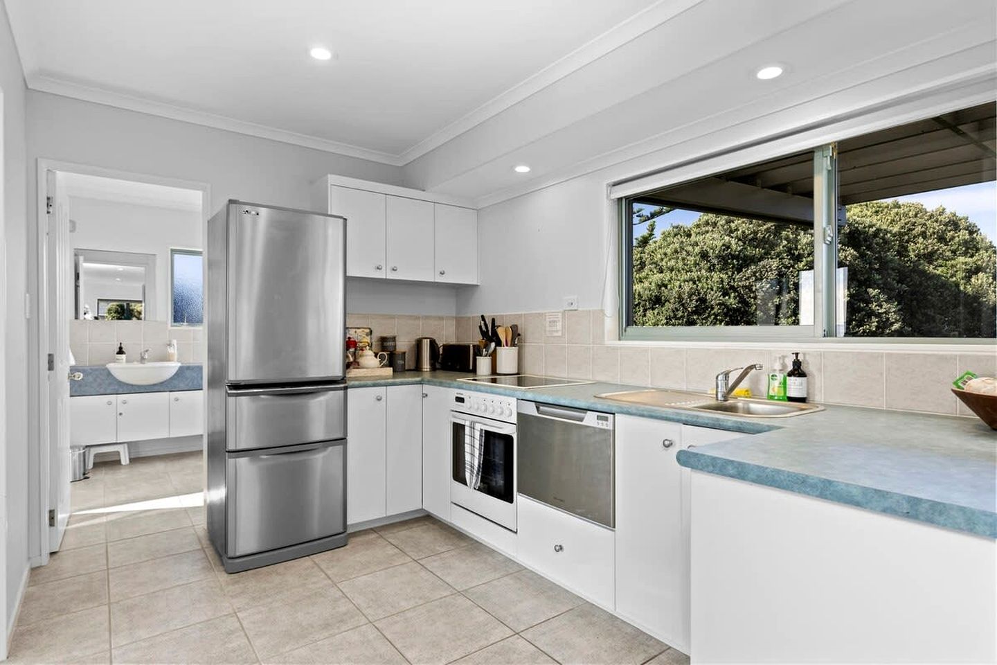 A modern kitchen with stainless steel appliances, white cabinetry, and a large window offering a view of greenery.