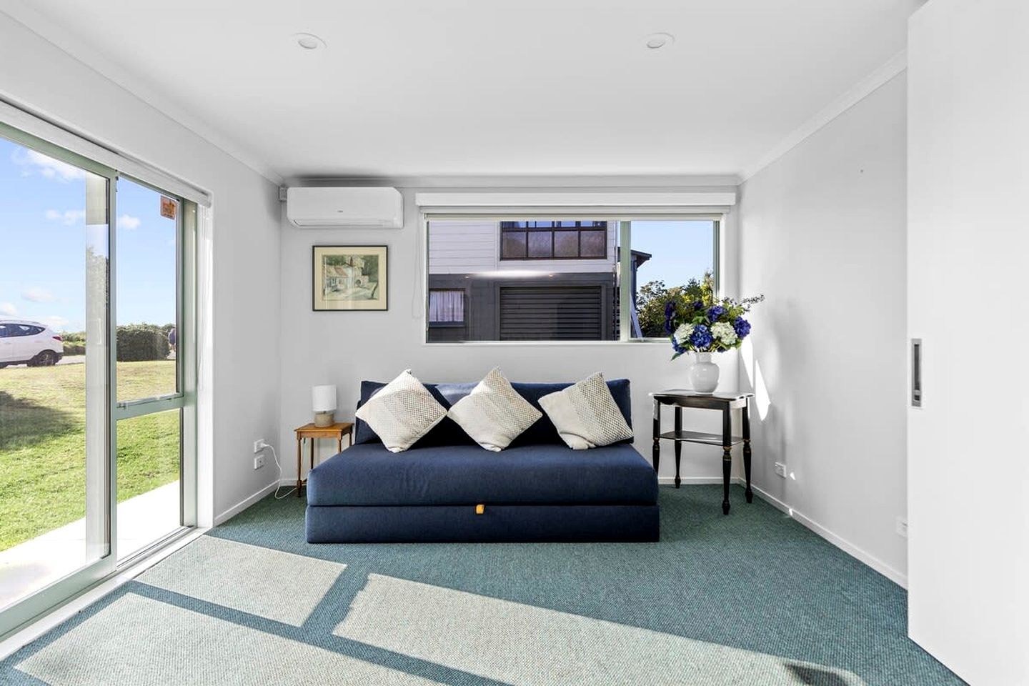 Una habitación con un sofá azul, una mesita con un jarrón y una ventana con persianas.