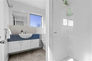 Een moderne badkamer met een wit wastafelmeubel, een blauw aanrecht en een douchecabine met glazen wanden.