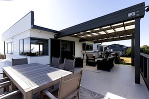 Een modern terras buiten, met een houten tafel en stoelen, een overdekte zithoek en uitzicht op het omliggende landschap.