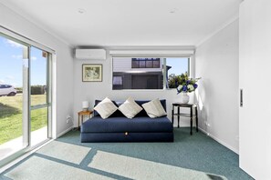 Ein Zimmer mit einem blauen Sofa, einem kleinen Tisch mit einer Vase und einem Fenster mit Jalousien.