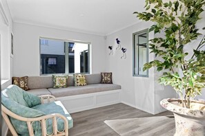 A room with a built-in bench, a wicker chair, a potted plant, and a window with a view. - Stunning Beachfront Holiday Home with Dual Sun Decks Near Waihi Beach Village | Waihi Beach, Bay of Plenty (Waihi Beach)